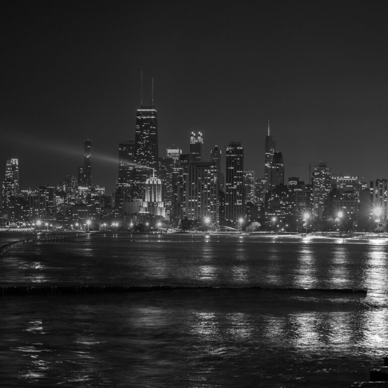 Black and white image of the Chicago skyline. Lake Michigan can be seen in the foreground.